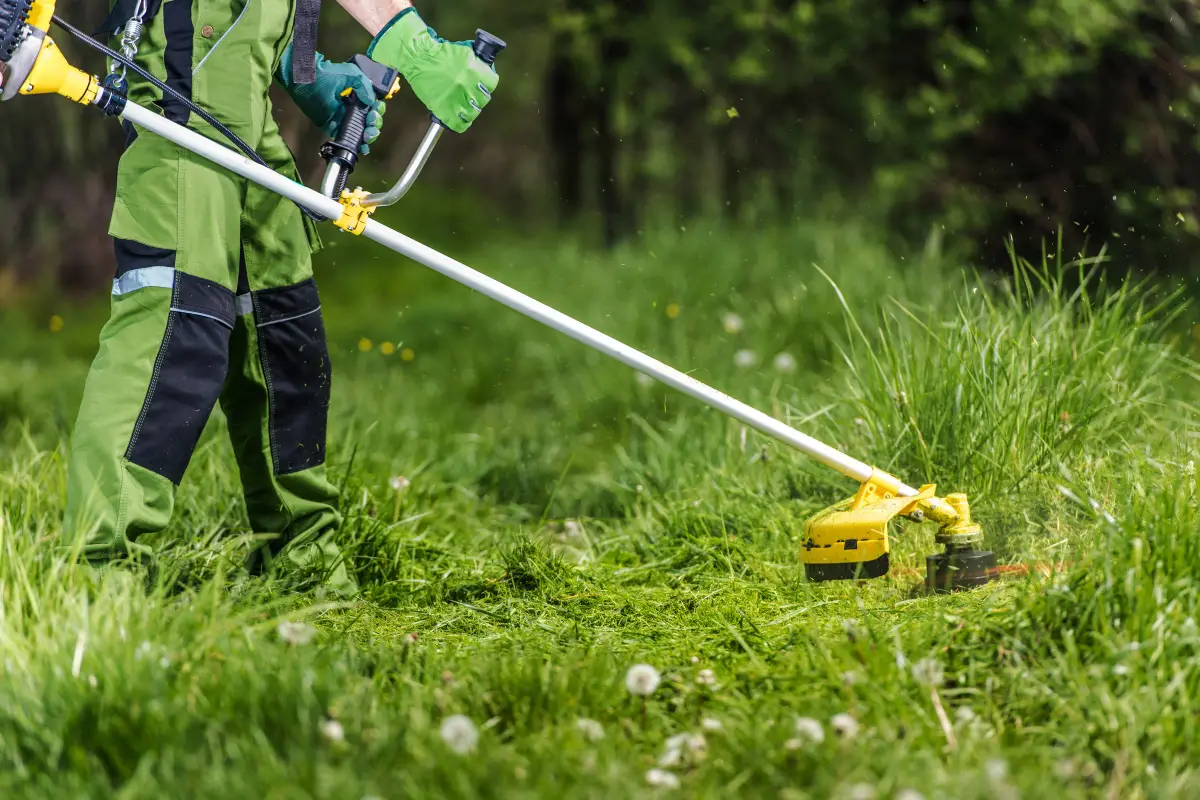 Lawn care technician trimming tall grass with a string trimmer